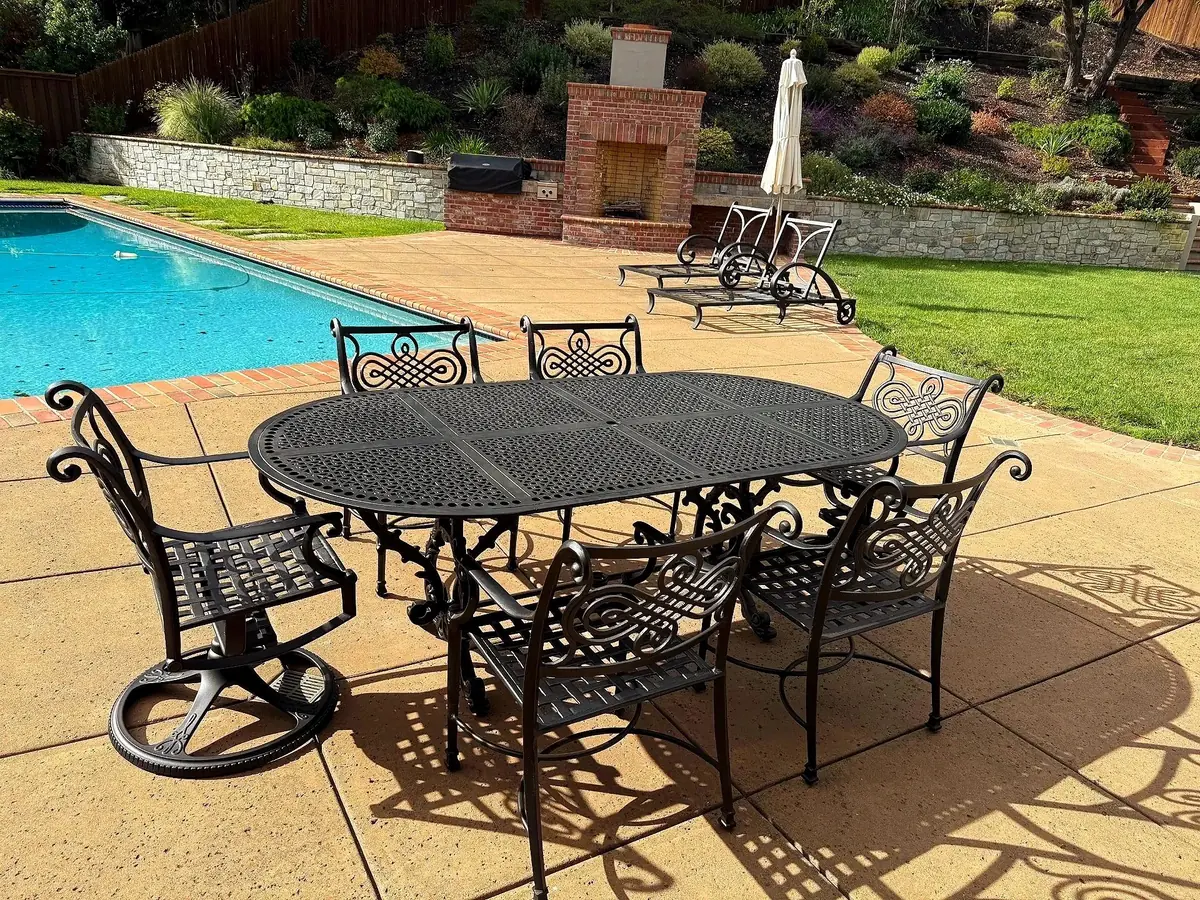 Restored black cast-aluminum patio dining set beside a pool and stone fireplace in a Bay Area backyard